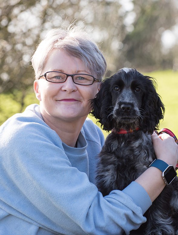 Woman with glasses holding a black dog outdoors